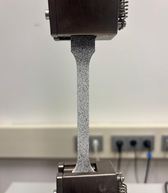 Aufgebrachter Speckle-Kontrast auf dem Zugprüfkörper zur digitalen Bildkorrelation (DIC). Das zufällige, hochkontrastreiche Muster bildet die Grundlage für eine robuste Korrelationsanalyse und die lokale Bestimmung von Verschiebungs- und Dehnungsfeldern während der Zugprüfung.